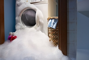Soapy water leaking from a white washing machine in a blue laundry room.
