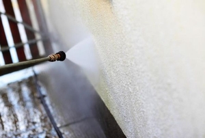Spraying a stucco wall with a pressure washer.
