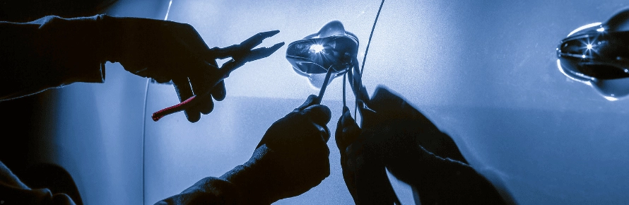 Photograph of an auto burglar using tools to break into a car at night.
