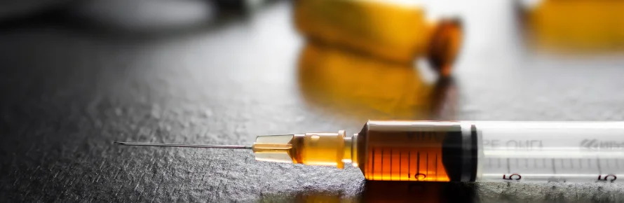 Photograph of ketamine in a syringe with blur image of glass bottle on dark table.