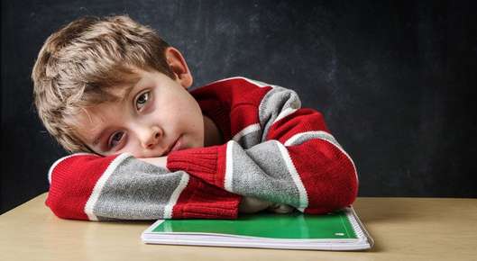 Image of a boy laying his head on his arms while sitting at a desk.