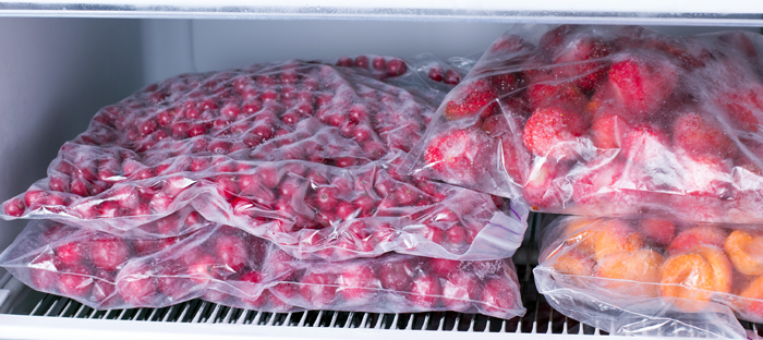 bags of frozen cherries, strawberries, and oranges on a freezer shelf