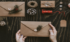 A pair of hands holding a kraft paper envelope surrounded by diy supplies for making holiday cards.