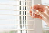 a hand closes window blinds on a sunny day