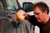 A disgruntled man applies elbow grease to his car.
