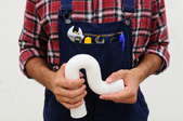 A plumber in overalls and a plaid shirt with holding a white pipe.