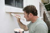 Painter at work applying white to the exterior of a home.