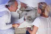A man and woman look at mold on a basement wall.