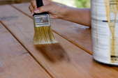 Using a brush to apply stain to outdoor wooden furniture.