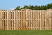 A scalloped wooden fence in a lush green backyard against a bright blue sky.