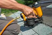 Man using a pneumatic nail gun to attach roofing materials