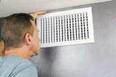 A man checking an air vent on a wall. 