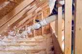 Side view of a man spraying cellulose insulation into a triangular space on one side of an attic.
