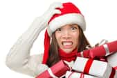 A woman wearing a Santa house and holding Christmas presents with a stressed look on her face.