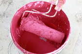 used paint roller in bucket of pink paint