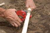 Close up of a man's hands cutting a piece of PVC irrigation pipe.
