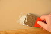 A closeup of a putty knife spreading spackle on a wall.