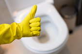 A hand in a yellow glove giving the thumbs up sign in front of a toilet.