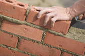 A worker laying bricks into mortar to create a brick wall.