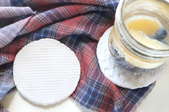 A pair of clay coasters with a drink on top and a flannel tablecloth. 
