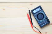 A black multimeter with a red and black probe lays on a wood surface.