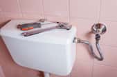 A toilet tank with tool on top against a pink wall.