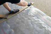 hands cutting plastic sheeting along a wooden frame