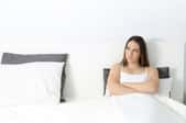 confused woman in bed near white wall