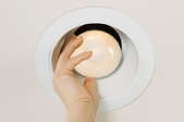 A recessed light with a hand adjusting the bulb.
