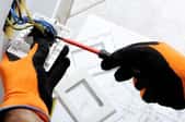 gloved hands working with the wiring of a power outlet