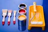 Three cans of paint, three brushes, a paint tray, and a roller sit on a blue surface.