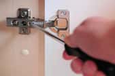 unscrewing cabinet door hinge with screwdriver