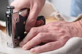 A staple gun being used to secure fabric to a wooden backing.