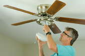 A man installing a ceiling fan. 