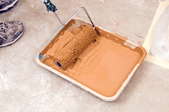 A paint roller pan full of light brown paint sitting on a concrete surface.