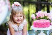 happy little girl with pink cake, roses, and trees in the background