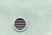 a mint green stucco wall with a circular vent