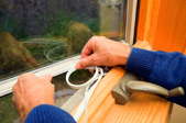 Applying rubber weather seal tape to a home window frame to prevent winter drafts and summer heat loss.