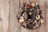 A rustic pine cone wreath against a wood background. 