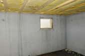 An empty basement with moisture stains on the wall and insulation in the ceiling. 