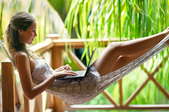 A young woman working on her laptop in a hammock