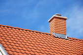 A red tiled roof with a brick chimney, topped with a chimney cap.