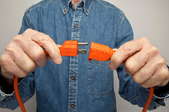 A man wearing a blue shirt plugging in an orange cord.
