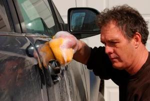 A disgruntled man applies elbow grease to his car.