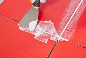 A putty knife scraping grout on red tile.