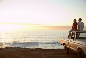 A couple sitting on a truck looking out on an ocean view.