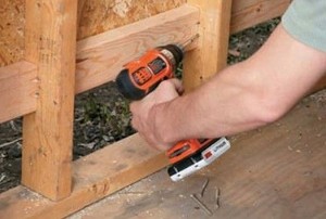 a man drilling new wood onto the bottom of a shed