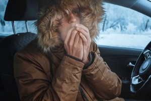 cold person in jacket in car blowing on hands