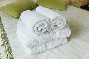 A stack of white bath towels on a bed with green pillows.