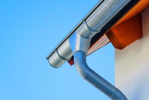 The intersection of a metal gutter and drain pipe on the corner of a house.